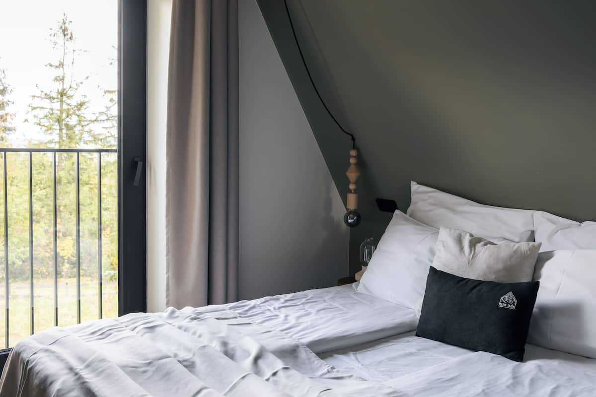 A neatly made bed with white linens, a dark pillow, and a window with curtains.
