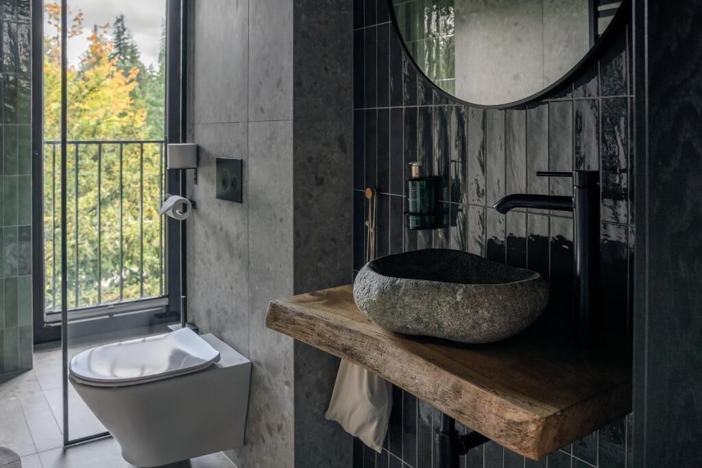 A modern bathroom with a freestanding bathtub, a stone basin sink, and a large mirror.
