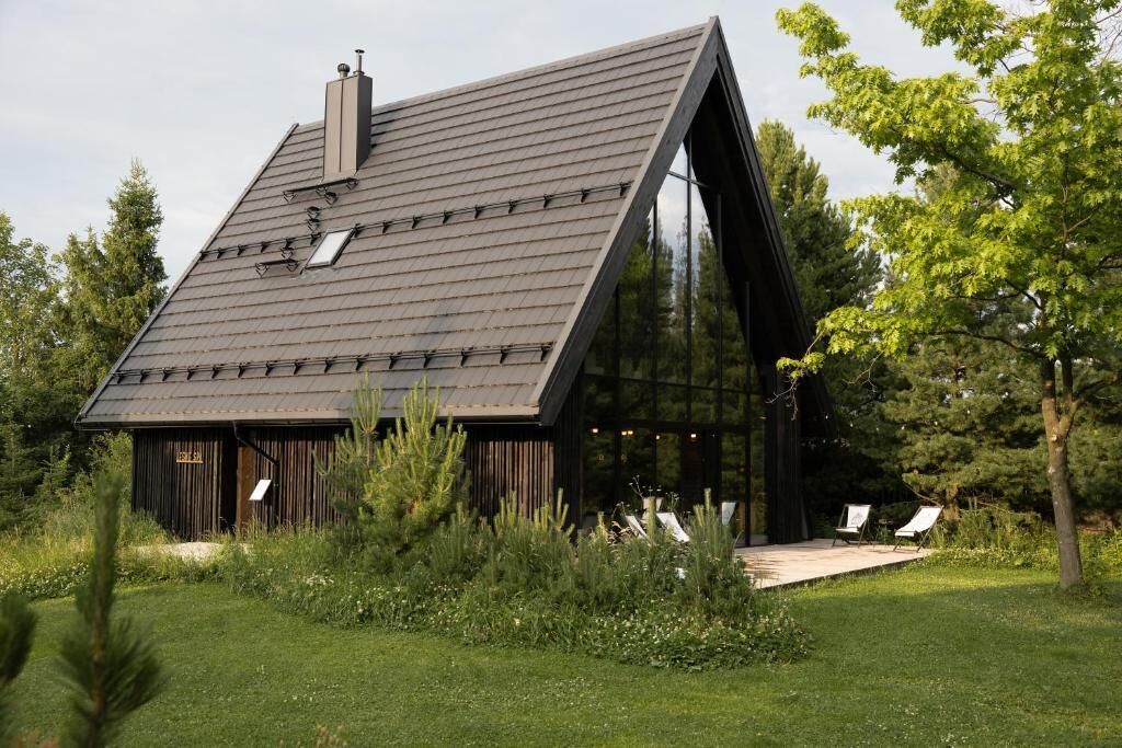 Una casa moderna con techo inclinado, ventanas amplias y una terraza de madera con sillas.