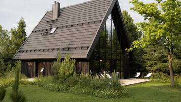 Una casa moderna con techo inclinado, ventanas amplias y una terraza de madera con sillas.