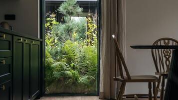 Una habitación con puerta corrediza de vidrio que da a un jardín exuberante, una silla de madera y un mueble verde.
