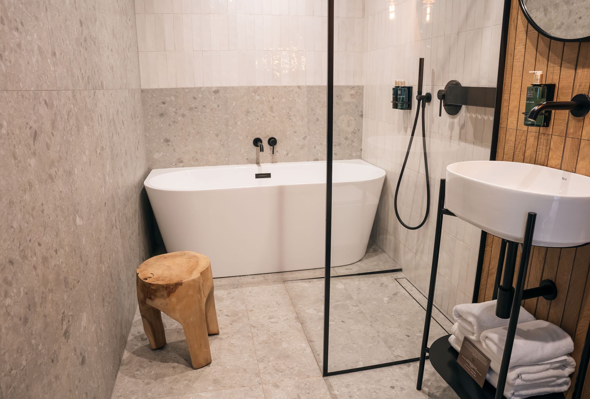 Une salle de bain moderne avec une baignoire sur pieds, un tabouret en bois, un lavabo avec un porte-serviettes et un mur recouvert de panneaux en bois.