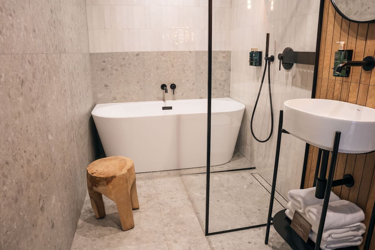 A modern bathroom with a freestanding bathtub, a wooden stool, a sink with a towel rack, and a wooden panel wall.