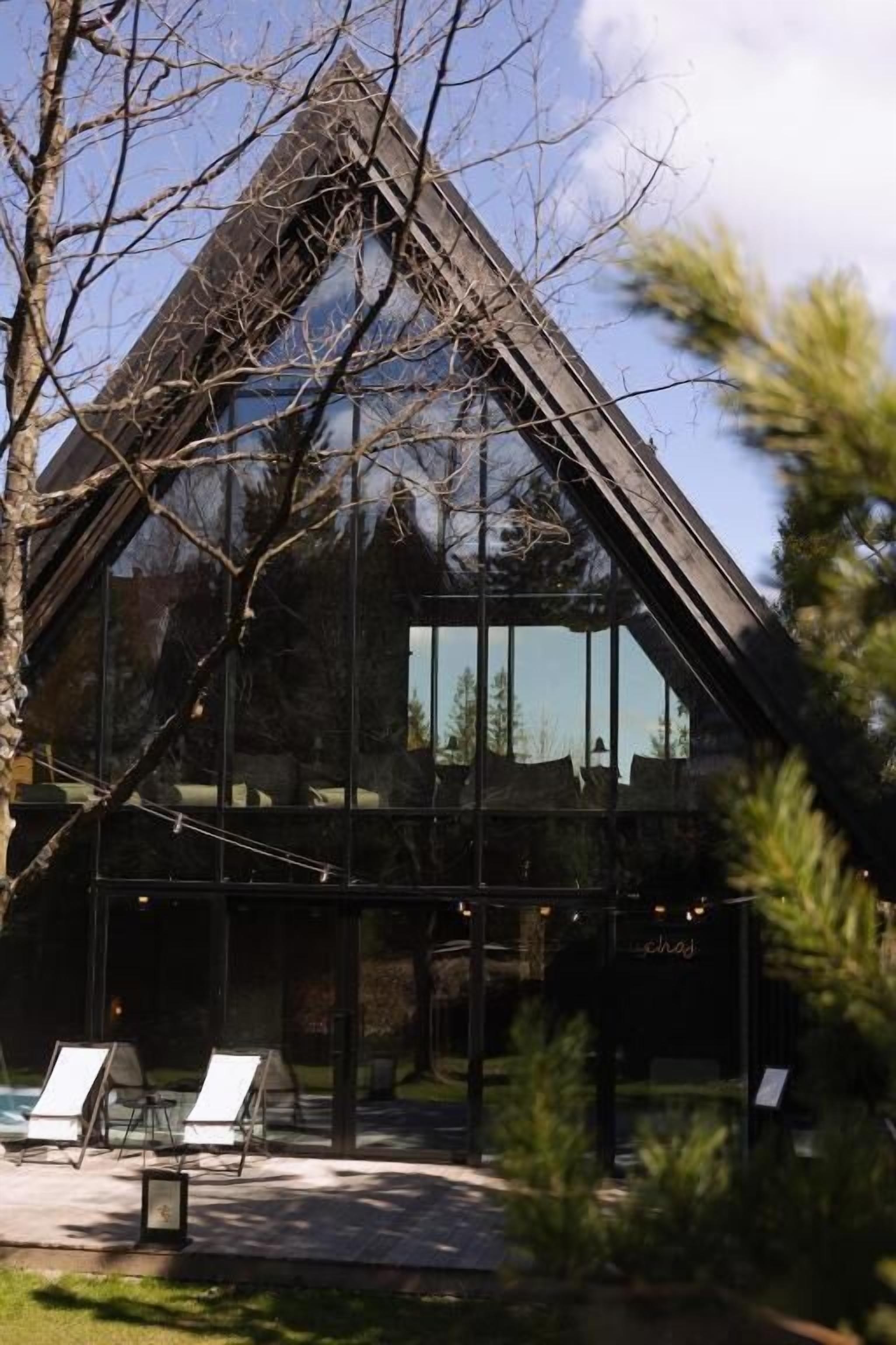 Un edificio moderno con techo triangular, ventanas grandes y mesas al aire libre.