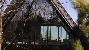 Un edificio moderno con techo triangular, ventanas grandes y mesas al aire libre.