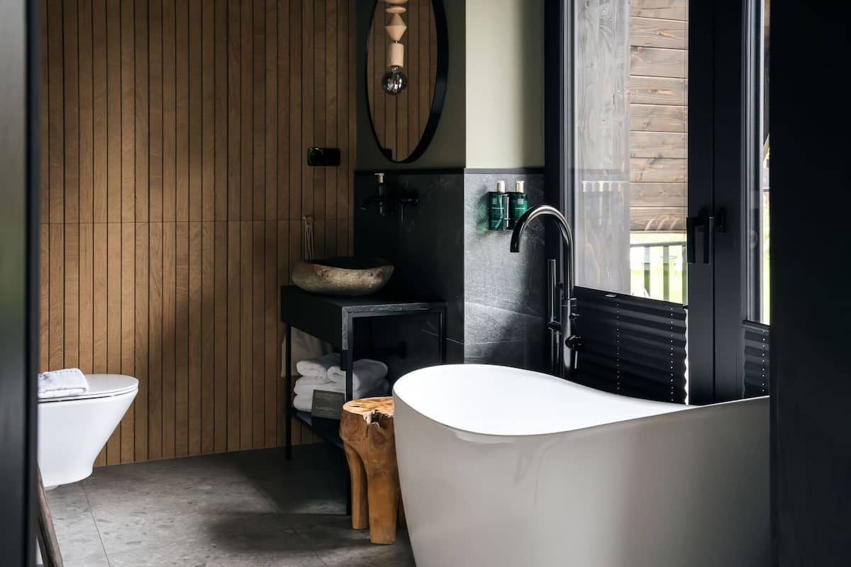 A modern bathroom with a freestanding bathtub, a wooden vanity, a round sink, and a toilet.
