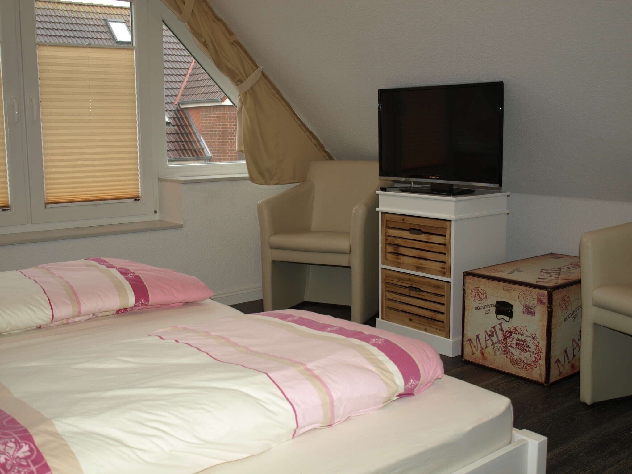 Une chambre à coucher avec un lit, un téléviseur posé sur un meuble, une chaise et une valise.