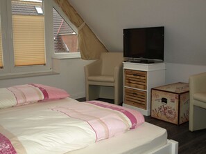 A bedroom with a bed, a television on a cabinet, a chair, and a suitcase. - Frisiastrasse – Holiday Apartment Seestern (Norden)