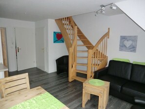 Ein Wohnzimmer mit einer Holztreppe, einem schwarzen Ledersofa, einem Holzesstisch und einem Teppich mit grünem Muster.