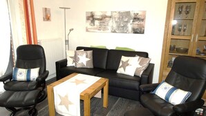 Ein Wohnzimmer mit einer schwarzen Couch, zwei schwarzen Sesseln, einem Holztisch und einer Vitrine.