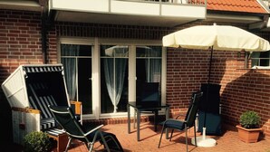 Eine Terrasse mit Tisch, zwei Stühlen, einer Liege und einem kleinen Blumentopf.