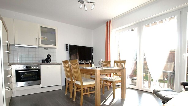 Eine moderne Küche mit Einbauofen, einem Esstisch mit Stühlen und einem großen Fenster mit Blick auf ein Gebäude.