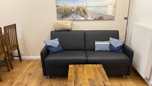 Ein schwarzes Sofa mit zwei Kissen, ein Holztisch und ein Gemälde mit einer Strandansicht an der Wand.