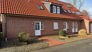 Ein rotbacksteins Gebäude mit geneigtem Dach, Oberlichtern und einem kleinen Gartenbereich mit Kies und Pflanzen.