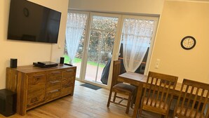 Ein Wohnzimmer mit Fernseher, Holzmöbeln, einem Esstisch mit Stühlen und einer Uhr an der Wand.