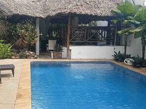 A swimming pool with a thatched roof structure, surrounded by potted plants and a bench. - Oasis Villa at Palm Park a tropical holiday home in the Indian Ocean (Ukunda)