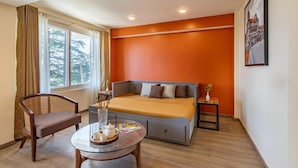 A room with a bed, a chair, a table with a tray, and a window with curtains. - Alaya Stays 1BHK Baljees Melville Utopia (Shimla)