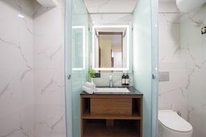 Ein Badezimmer mit Marmorwand, einer Glaskabine zur Dusche, einem hölzernen Waschtisch und einer weißen Toilette.