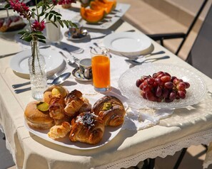 Une table de petit-déjeuner avec des viennoiseries, un verre de jus d’orange et une assiette de raisins.