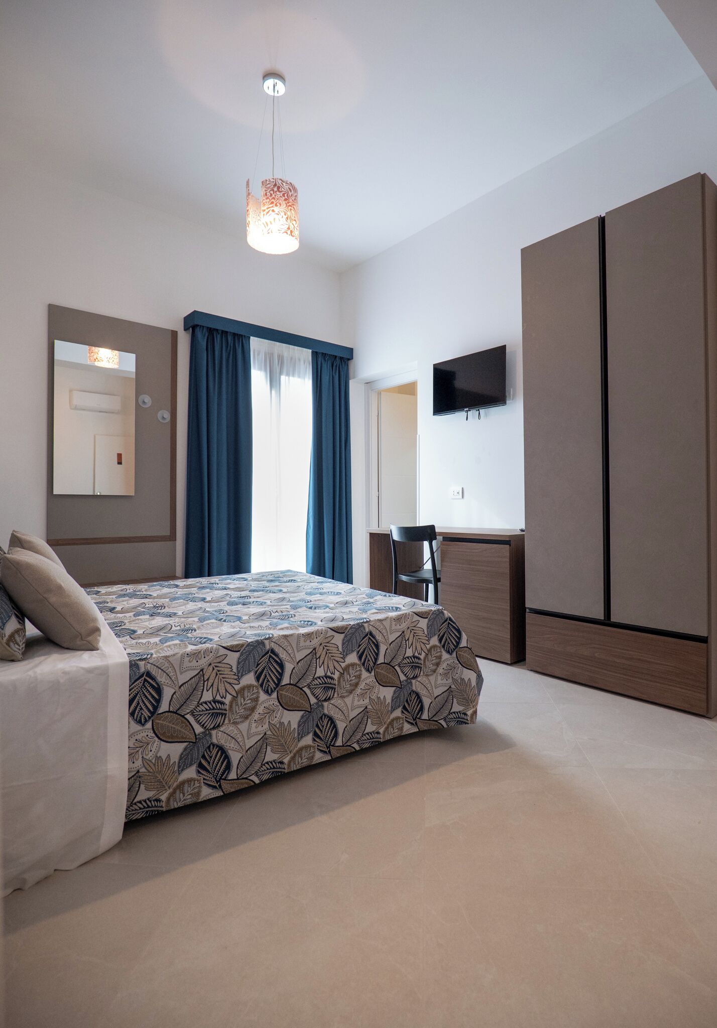 A bedroom with a bed, a desk, a TV, and a wardrobe.