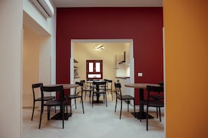 A dining area with multiple tables and chairs, a red accent wall, and a kitchen visible through an open doorway. - Monnalisa Rooms (San Vito Lo Capo)