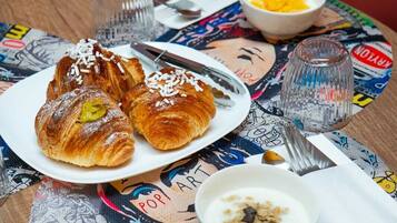 Une table avec des croissants, un bol de yaourt agrémenté de granola, un verre d’eau et une cuillère.