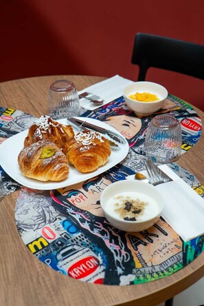 Une table avec des croissants, un bol de yaourt agrémenté de granola, un verre d’eau et une cuillère.