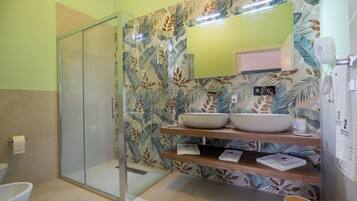Une salle de bain avec une douche à parois de verre, un grand miroir, deux lavabos avec des cuves, et une étagère en bois où sont posées des serviettes.
