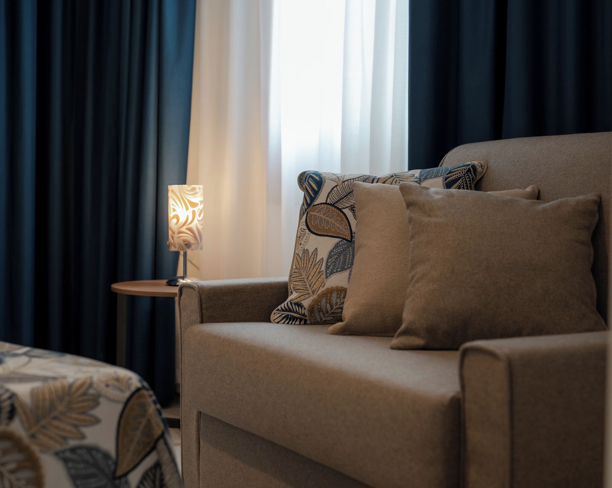 Una camera d'albergo con un letto, un divano, una lampada e una finestra con tende.