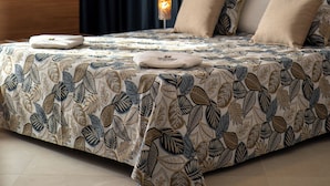 Een slaapkamer met een bed, donkere gordijnen, een bedlampje en beddengoed met een patroon.
