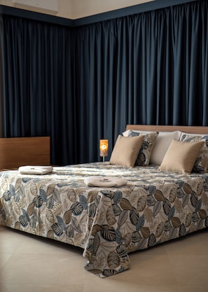 A bedroom with a bed, dark curtains, a bedside lamp, and patterned bedding. - Monnalisa Rooms (San Vito Lo Capo)