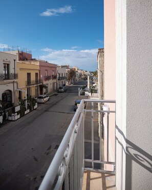 Une vue sur la rue depuis un balcon, avec des immeubles, un ciel dégagé et des voitures garées.