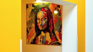 Een kamer met een gele muur en een groot abstract schilderij.