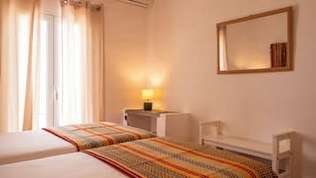 A hotel room with two beds, a bedside table with a lamp, a mirror on the wall, and a window with curtains.