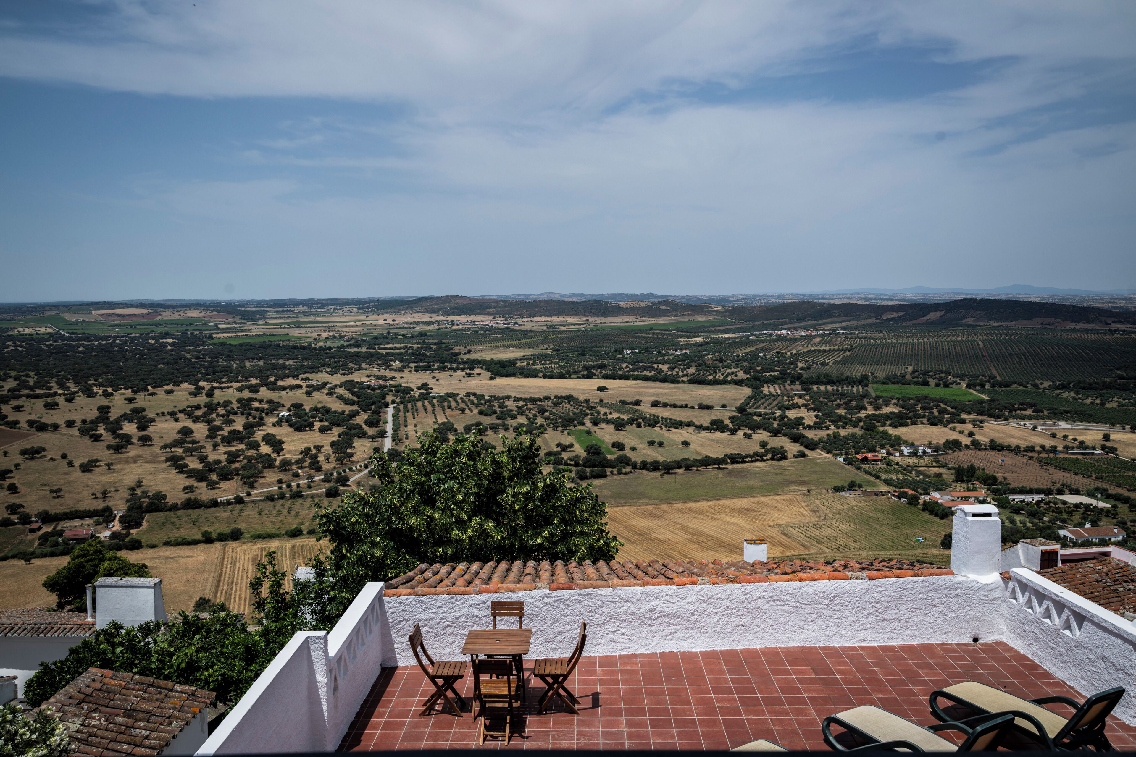 Une terrasse avec une table et des chaises, donnant sur un paysage rural composé de champs et d’arbres.