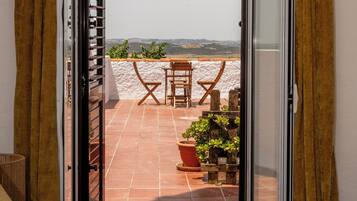 Une chambre à coucher avec un lit, une fenêtre et une vue sur un patio équipé d’une table et de chaises.