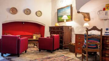 A room with a red sofa, a wooden chair, a small table, a lamp, and a painting on the wall.