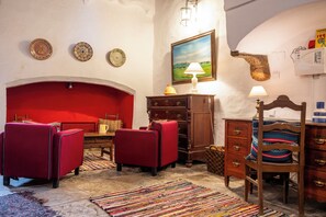 Una habitación con un sofá rojo, una silla de madera, una mesita, una lámpara y un cuadro en la pared.