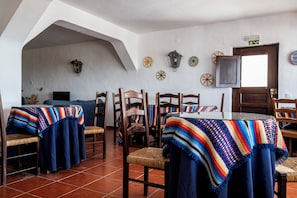 A dining area with wooden chairs and tables, a tiled floor, and a door with an exit sign. - Dom Nuno by Horta da Moura (Reguengos de Monsaraz)