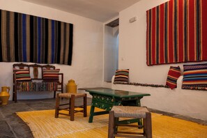 A room with a green table, wooden chairs, a bench with colorful cushions, and a yellow rug.