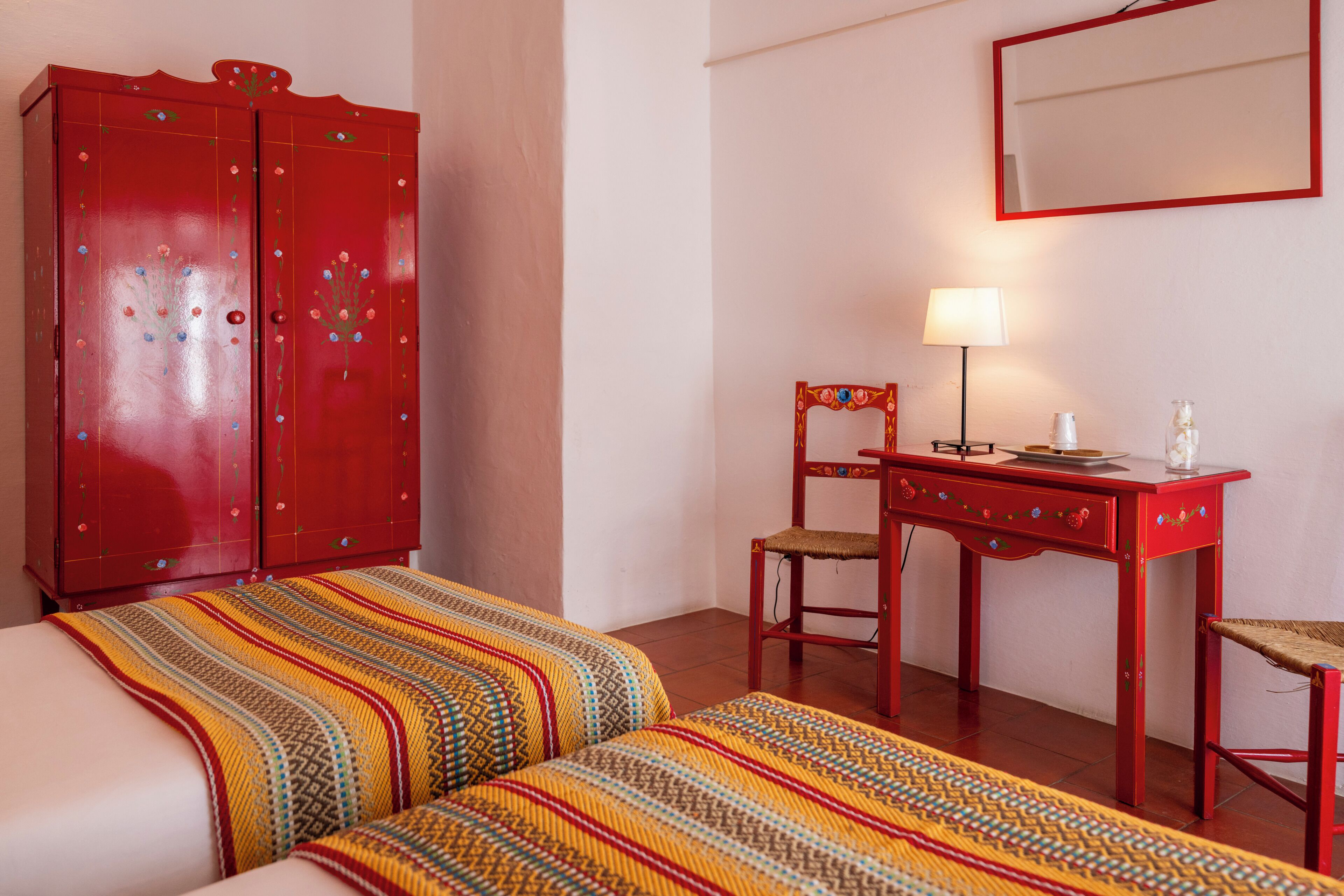 Une chambre comprenant un lit, un bureau avec une chaise, une armoire et une table de chevet avec une lampe.