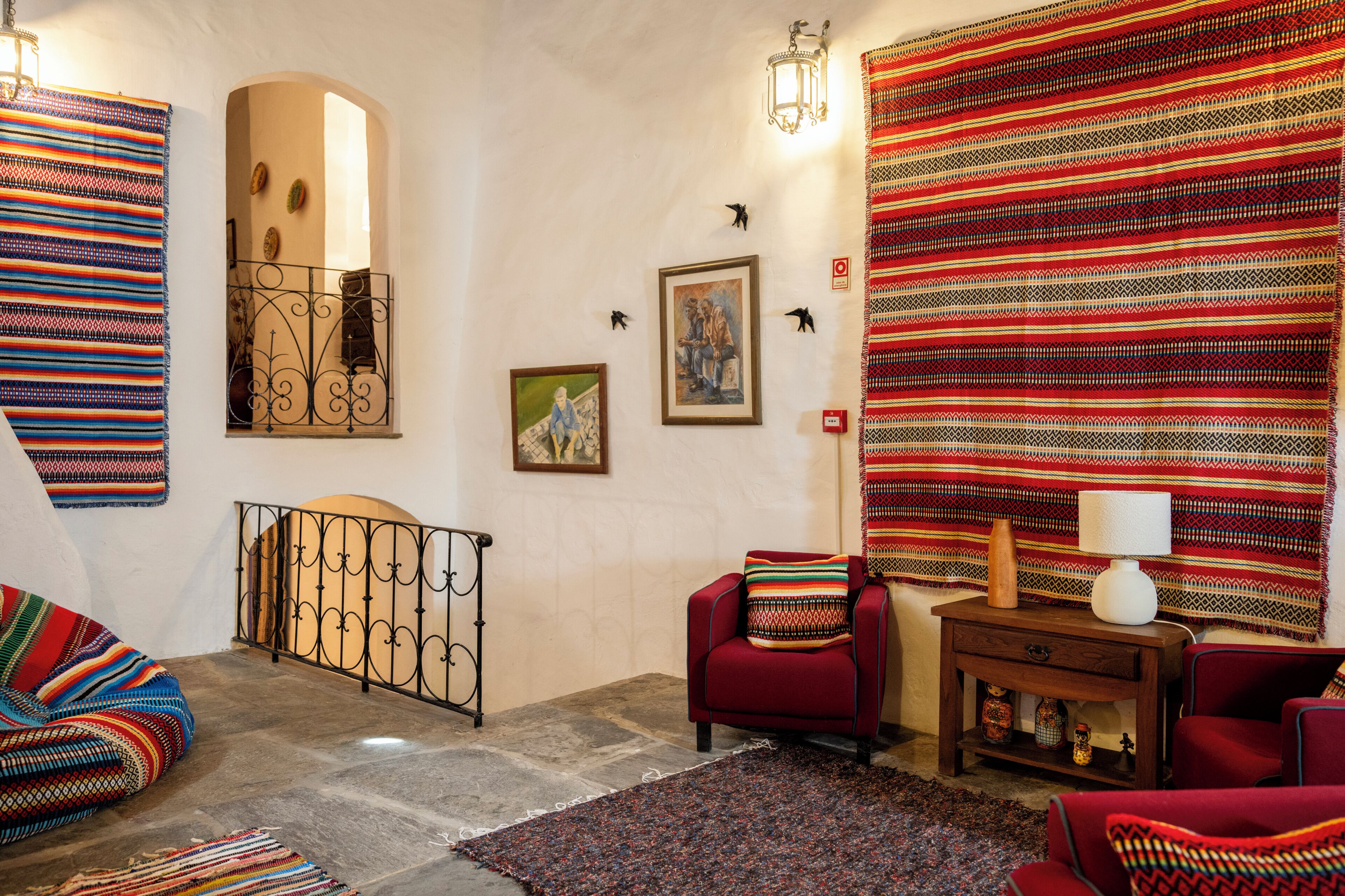 Una habitación con un sillón rojo, un tapete estampado y un gran tapiz en la pared.