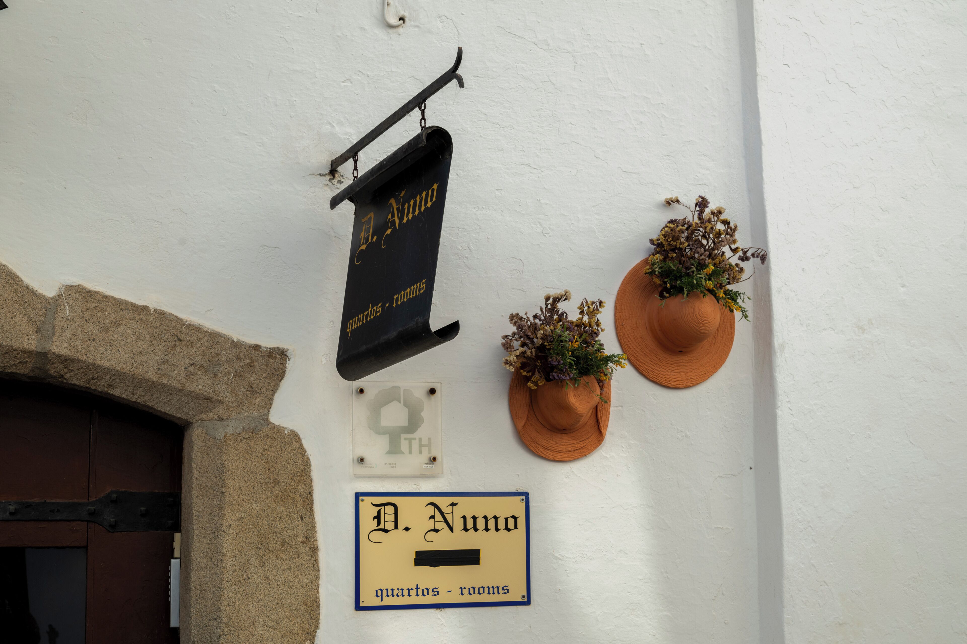A wall with signs indicating 'D. Numo quartos - rooms' and a door with a stone archway.
