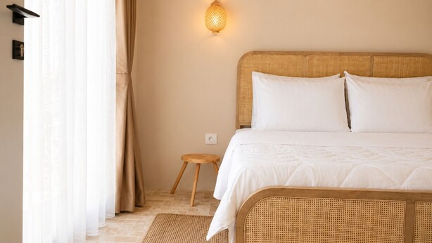 Une chambre à coucher comprenant un lit, une table de chevet, une lampe fixée au mur et une fenêtre avec des rideaux.