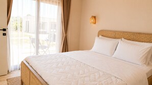 Une chambre d’hôtel avec un lit, des rideaux, une lampe fixée au mur et une vue sur l’extérieur.