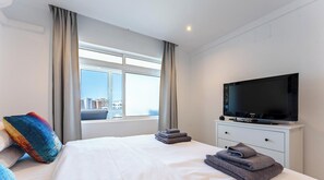 Ein Hotelzimmer mit Bett, Fernseher, Fenster mit Vorhängen und Blick auf Gebäude.
