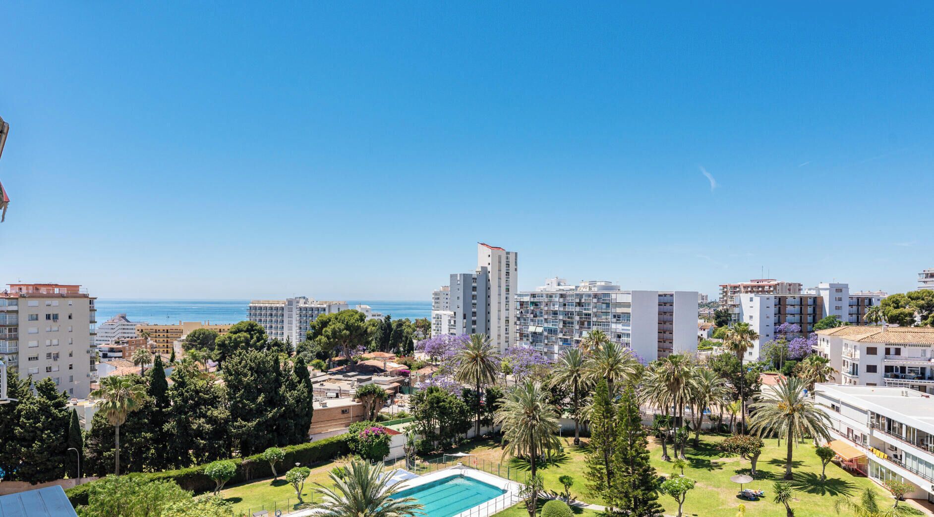 A coastal cityscape with modern buildings, a clear sky, and a swimming pool.