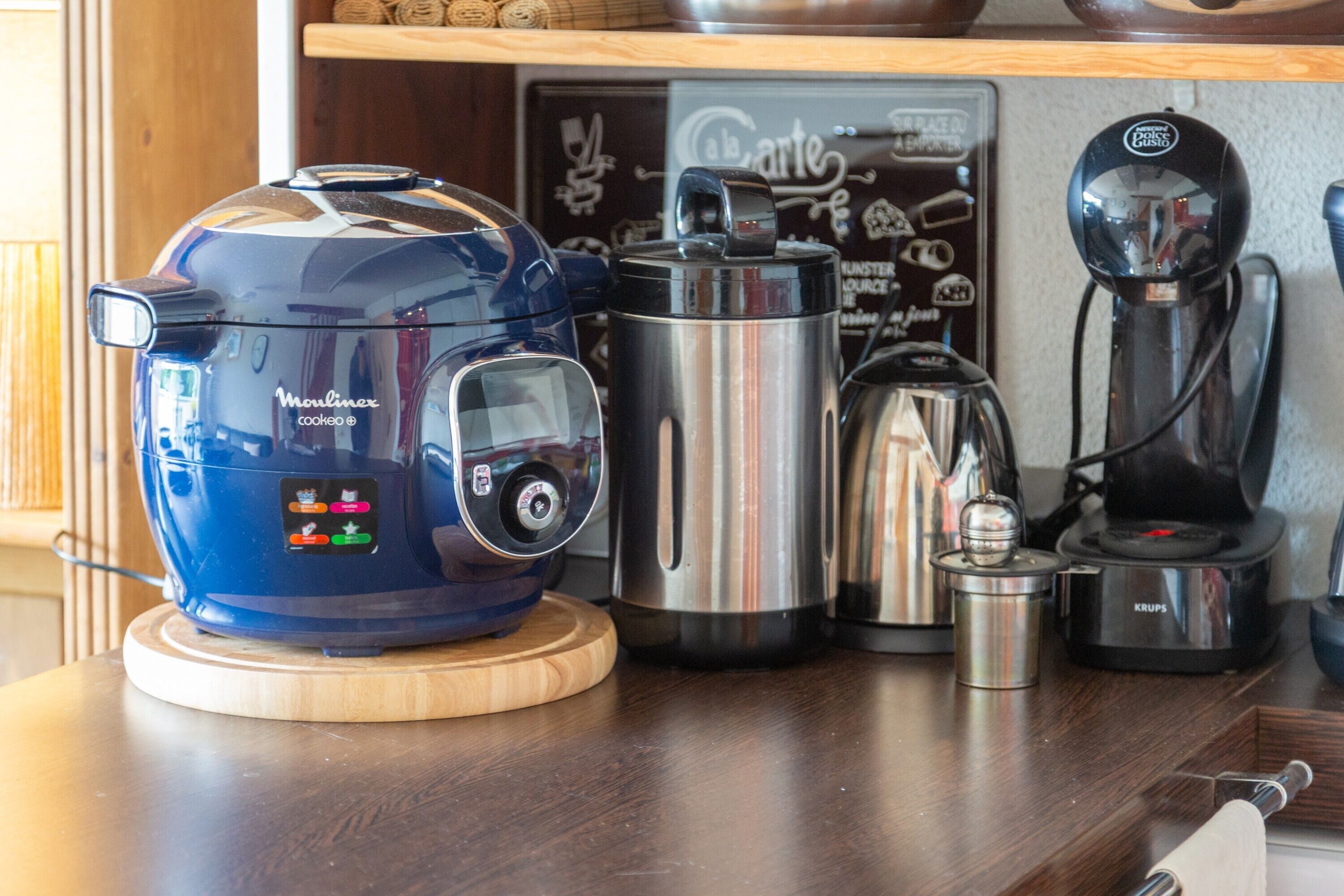 Eine Küche mit einem blauen Slow Cooker, einem Edelstahlkochtopf, einer Kaffeemaschine und einem Gerät von Krups auf einer Holzauskład.
