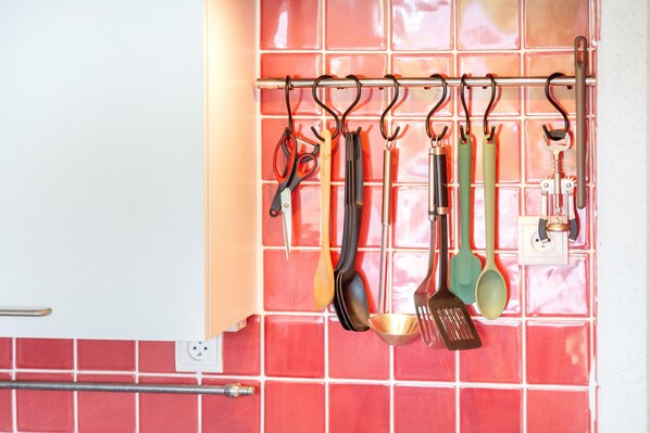 A kitchen with red tiles, a hanging utensil rack, and a white cabinet.