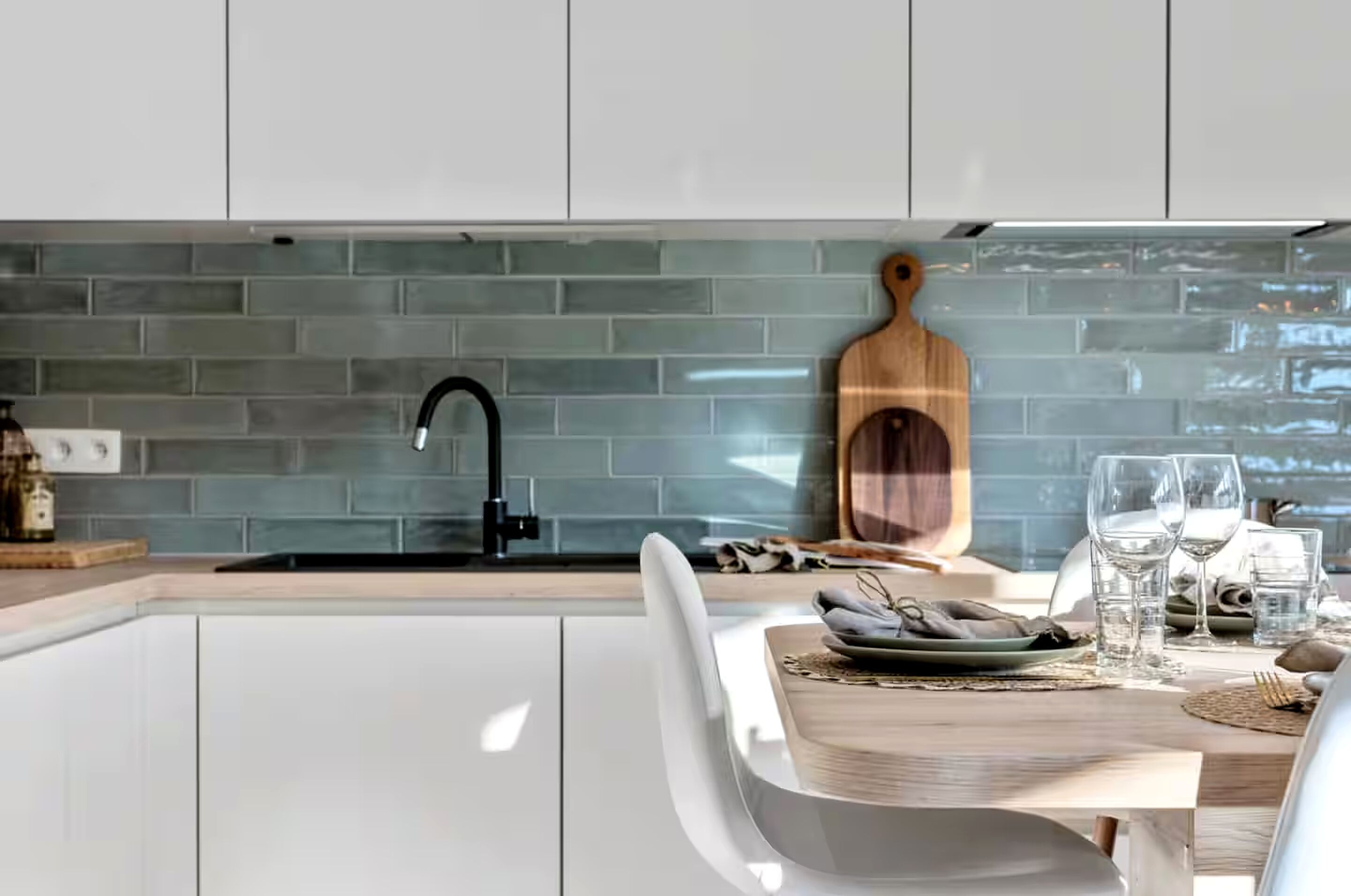 Una cucina moderna con mobili bianchi, una parete backsplash in piastrelle blu, un rubinetto nero e un tagliere di legno.